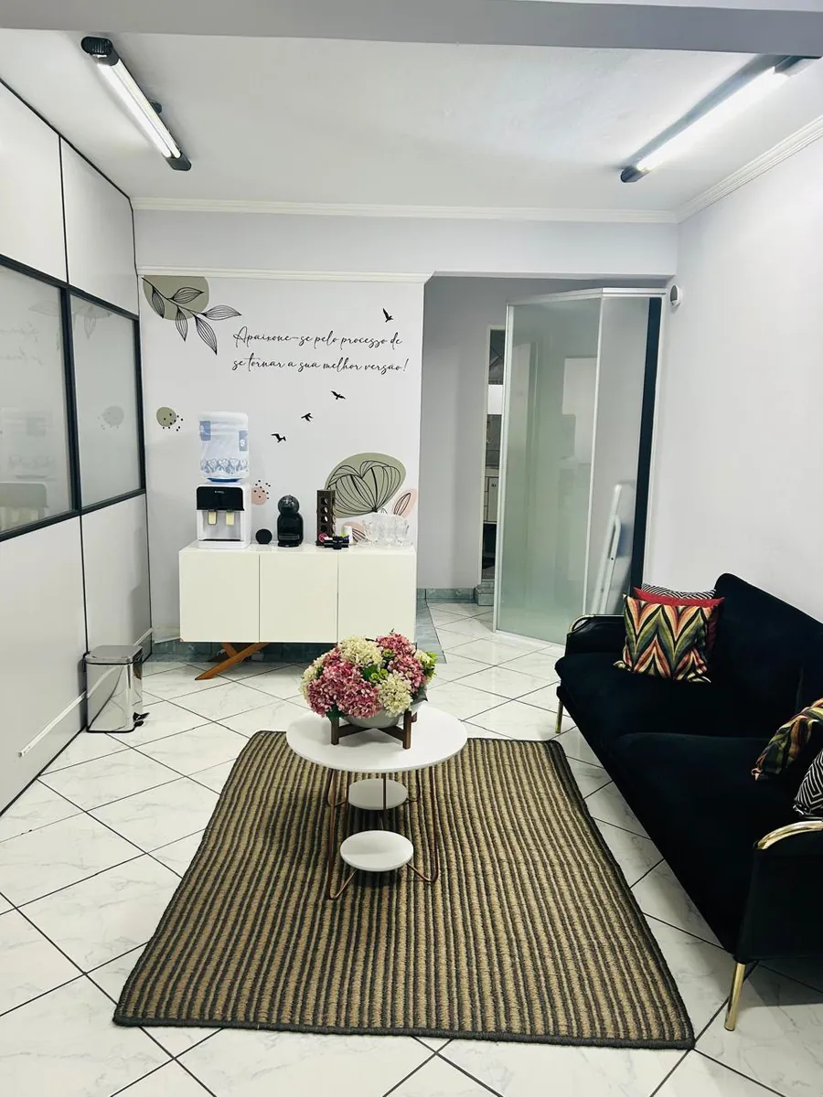 Sala de espera com sofá, tapete e flores no consultório de Jandira