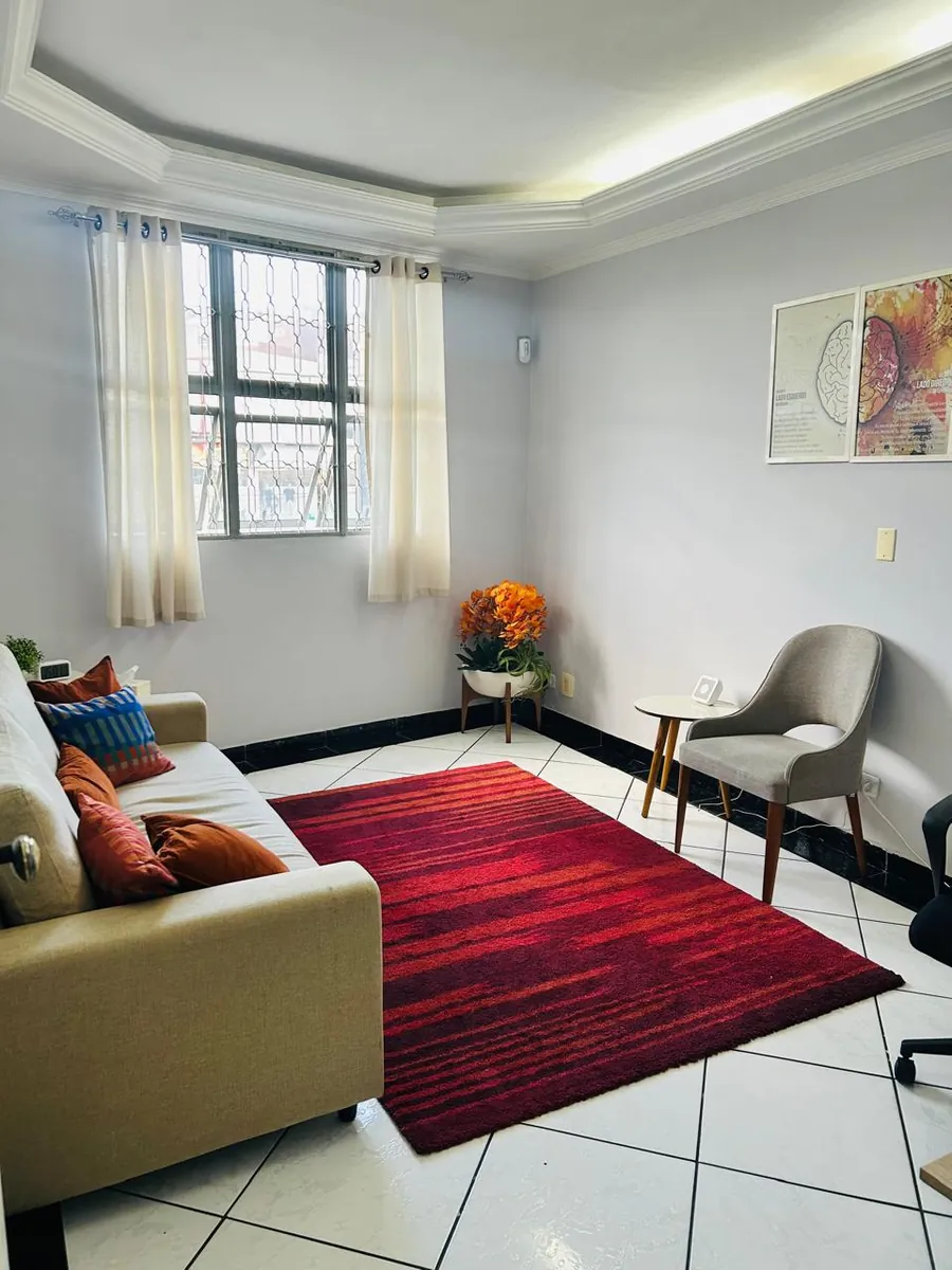 Sala de atendimento com sofá, poltrona e tapete vermelho em Jandira